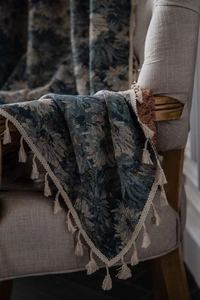 Close-up of vintage floral woven throw blanket with tassels on a brown fabric armchair