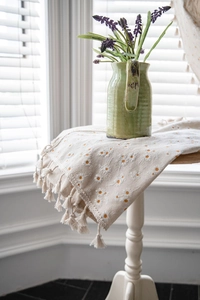Detail of beige cotton linen table runner with daisy embroidery and fringed edges