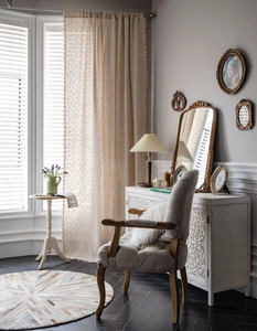 Detail of beige floral linen curtain with tassel trim and vintage French armchair