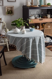 Detail of round gray-blue tablecloth with white embroidery and elegant fringe tassels