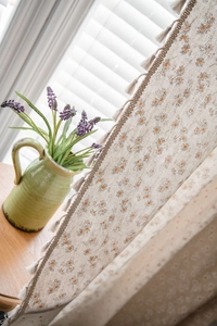 Detailed view of linen curtains featuring daisy floral print and elegant beige tassel trim