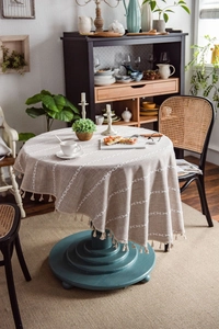 Detail of round linen-style tablecloth featuring white embroidery and fringe pompom edges