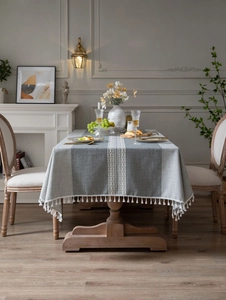Detailed close-up of blue-grey linen tablecloth with white woven stripes and fringe tassels