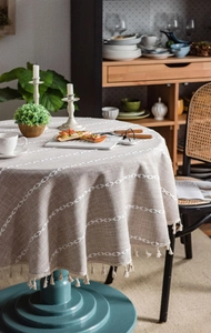 Close-up of beige linen round tablecloth featuring white leaf embroidery and fringe edges