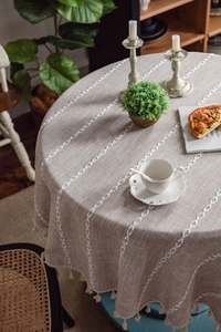Detailed close-up of beige round tablecloth featuring leaf embroidery and tassel edges
