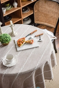 Detailed macro view of beige faux linen round tablecloth with white floral embroidery and fringe