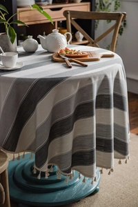 Close-up of grey striped round tablecloth with elegant beige tassels in a home setting