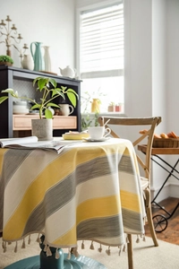 Detail of yellow and grey striped round tablecloth with elegant beige fringe tassels