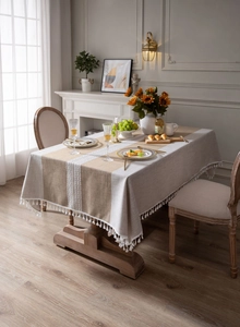 Detail of brown faux linen tablecloth with grey patchwork, white lace, and pom-pom fringe