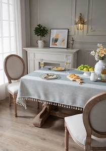 Detail of grey linen-textured tablecloth with white pom pom fringe on a wooden table