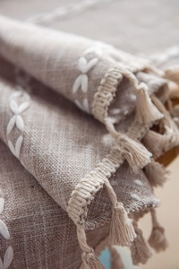 Close-up of linen tablecloth featuring white geometric embroidery and delicate tassels