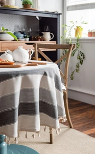 Close-up of grey striped cotton linen tablecloth with decorative tassel fringe on round table