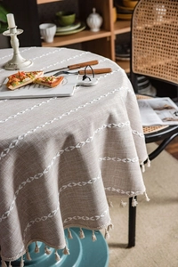 Close-up of beige linen tablecloth featuring white embroidery and elegant tassel fringe