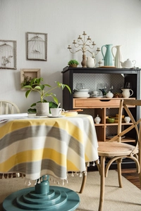 Detail of round yellow striped tablecloth featuring elegant off-white tassel fringe edges