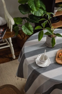 Detail of round grey striped tablecloth with tassel fringe and Nordic home decor setting