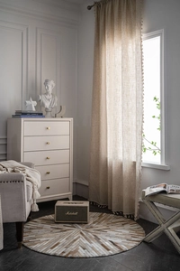 Detail of beige linen curtain with decorative pom-pom tassels in a cozy living room setup