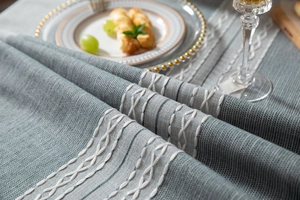Detailed close-up of gray-blue linen textured tablecloth with white cross-stitch embroidery