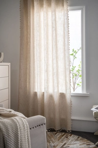 Detail of light beige linen textured curtain with decorative mini fringe pom-poms