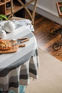 Detailed top view of grey striped round tablecloth with elegant tassel edges in a cozy home