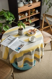 Detail of round yellow striped tablecloth with beige pom-pom tassels in a cozy home setting