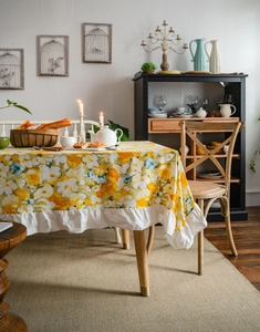 Detail of yellow floral tablecloth with white ruffled edge in a rustic dining setting