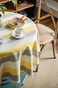 Detail of round yellow striped tablecloth with elegant tassels in a cozy dining setting
