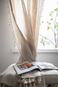 Close-up of beige linen curtain fabric featuring elegant fringe tassels and natural fiber texture