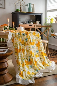 Detail view of yellow floral tablecloth with elegant white ruffle edges in a cozy home setting