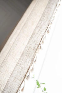 Detailed texture of beige linen fabric with elegant fringe tassels on curtain edges