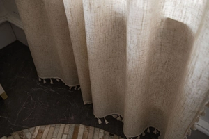 Detailed view of beige linen curtain with hand-woven tassel fringe and textured weave