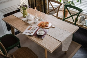 Close-up of cream floral table runner on solid white oak dining table in cozy home setting