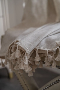 Close-up of natural linen curtain with handmade fringe tassels on a vintage chair
