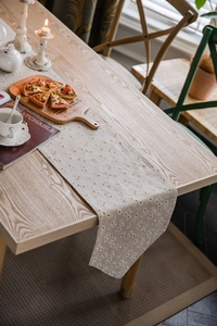 Detail of beige table runner with white daisy embroidery and orange polka dots on wood