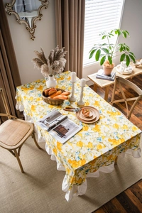Detail of yellow floral rectangle tablecloth with white ruffle edge and linen texture
