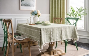 Detail of green linen tablecloth with white stripe embroidery and delicate tassel fringe