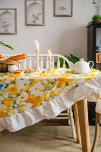 Close-up of yellow floral tablecloth with delicate white ruffled edges in a rustic dining setting