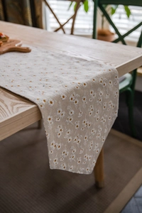 Close-up of beige table runner featuring white daisy floral prints on linen fabric texture