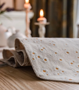 Detail of embroidered small daisies on cream-colored linen table runner over wood