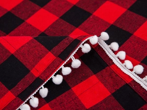Macro shot of red and black buffalo plaid fabric with white pom-pom decorative edges