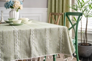 Detail of green cotton linen tablecloth with white woven stripes and fringe tassels