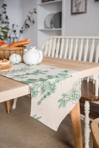 Linen table runner with green pine branch print on a natural wooden dining table