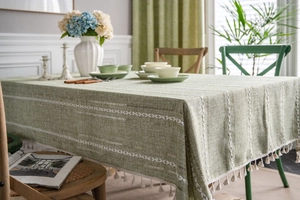 Detailed macro view of green cotton linen tablecloth with white ethnic embroidery and tassels