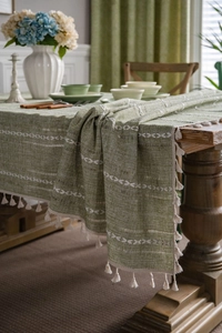 Macro detail of green cotton linen tablecloth with white ethnic embroidery and fringe