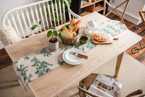 Linen table runner with green pinecone print displayed on a wooden dining table