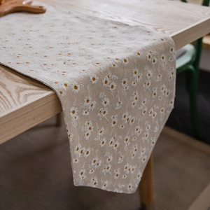 Linen table runner with white daisy floral print on a beige wooden dining table
