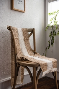 Detail of bohemian cotton linen table runner with woven tassels hanging on a wooden chair