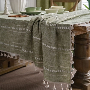 Green bohemian linen tablecloth with white geometric embroidery and tassels on wood table