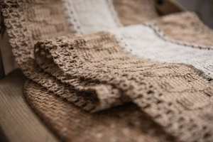 Close-up of rustic jute table runner with delicate crochet lace borders and tassels