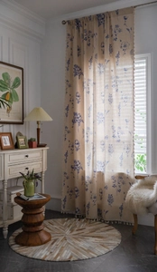 Close-up of blue floral print curtains with decorative fringe trim in a bright room