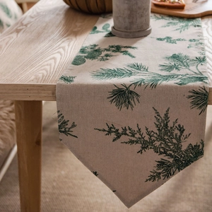 Linen table runner with green pine needle pattern on a natural beige wooden table